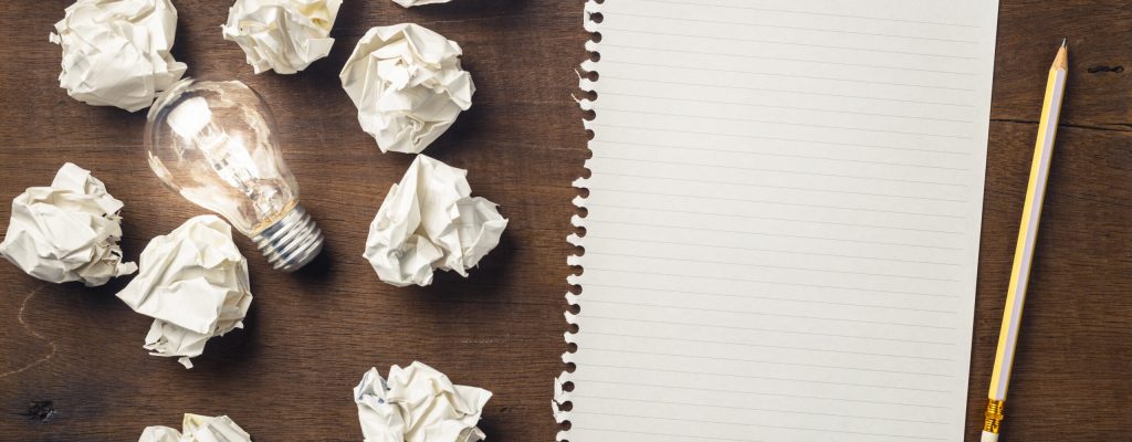 Paper and pencil with glowing light bulb among the crumpled rubbish for writing concept